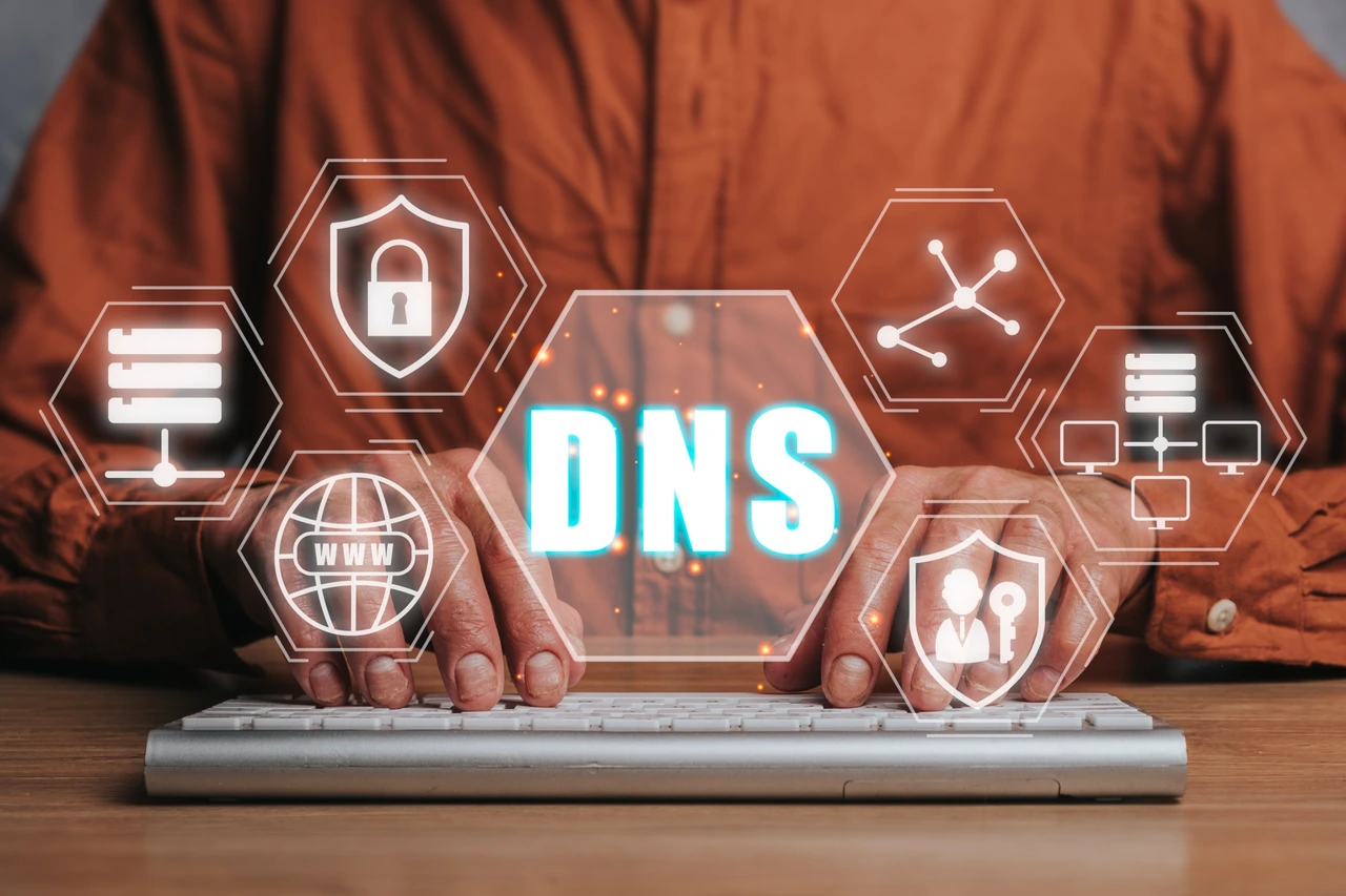 Hands type on a keyboard with the word “DNS” highlighted at the center, surrounded by icons.